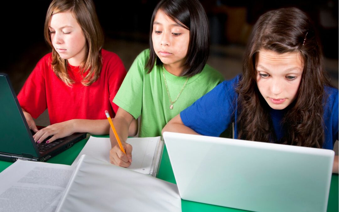 2 fillettes avec laptop entourent une autre avec cahier crayon