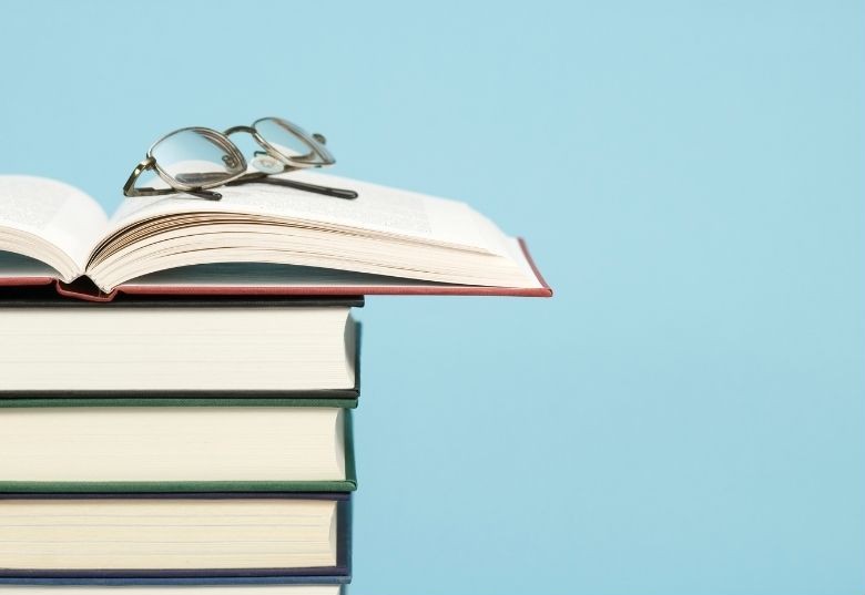 une pile de livres avec des lunettes posées sur un livre ouvert en haut de la pile